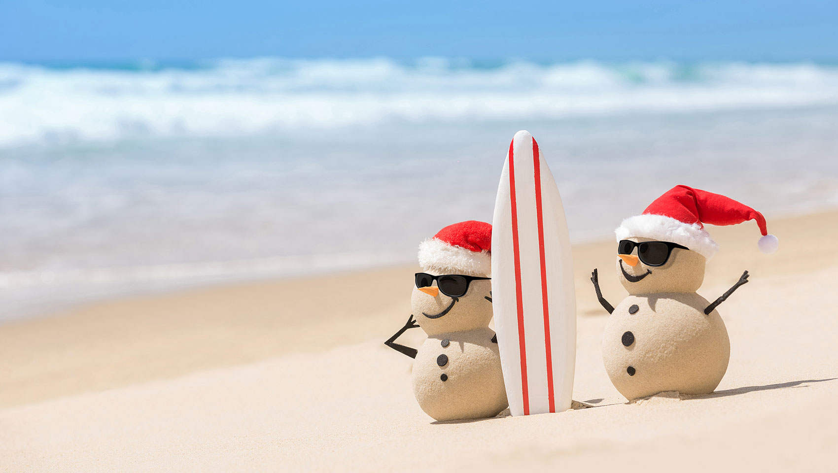 Sandy Snowmen on the beach with a surfboard