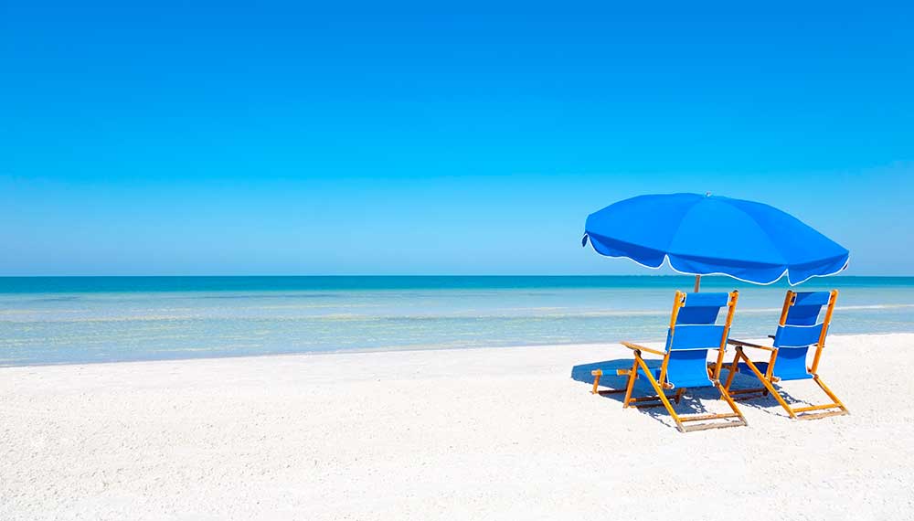 2 blue chairs + blue umbrella on a sandy beach on a sunny day