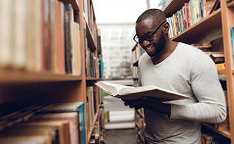 man reading a book while standing in a large library
